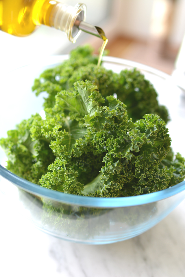 a hand pouring oil onto fresh kale leaves in a bowl