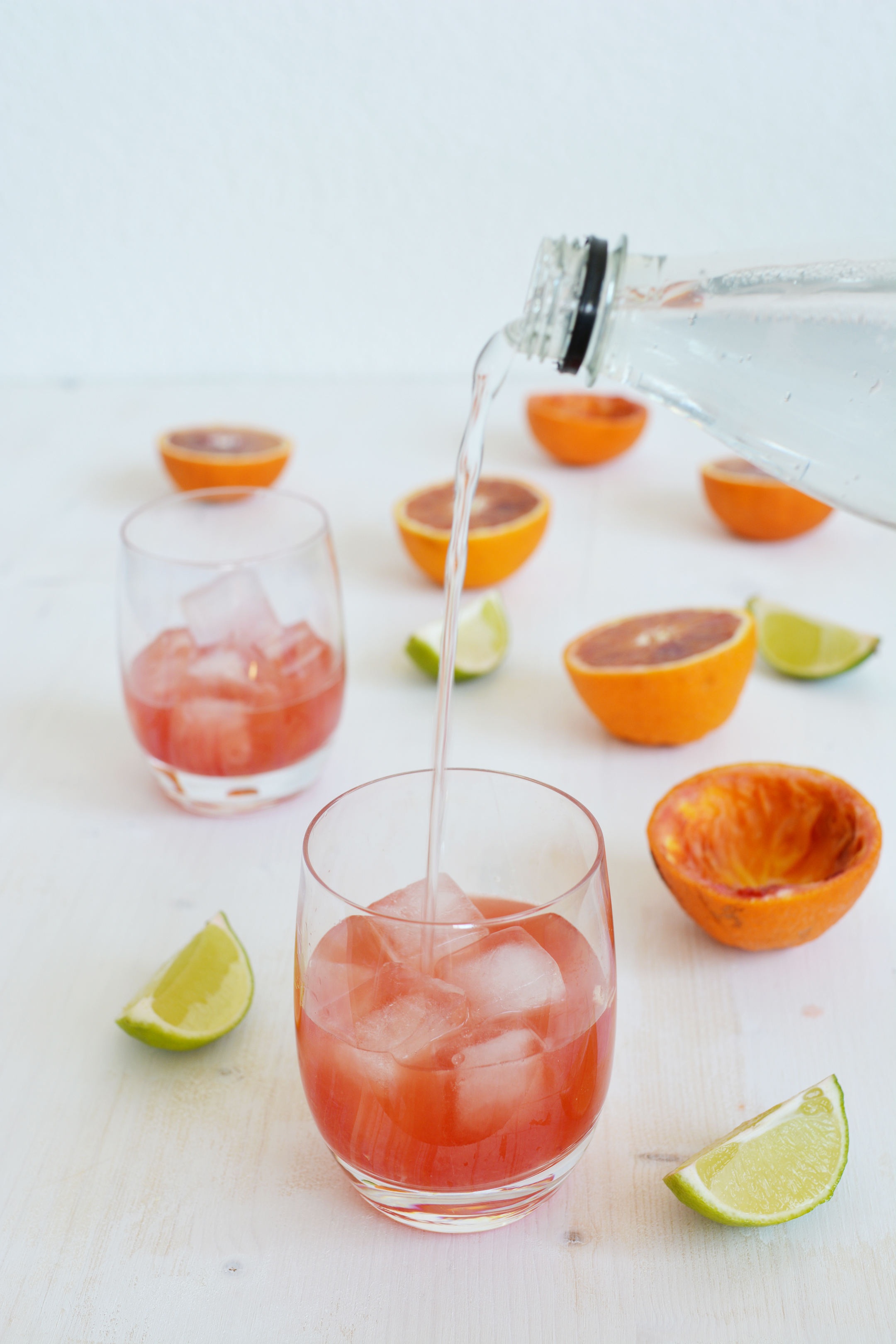adding of tonic water on the glass with gin and blood orange juice and ice.