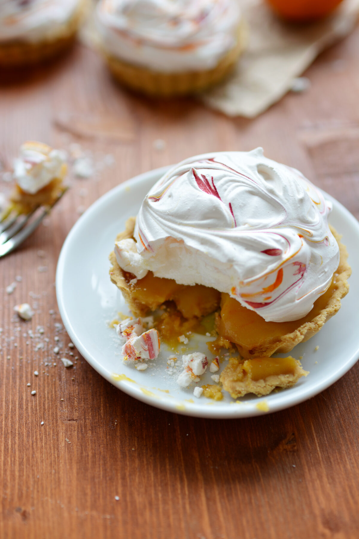 close-up view of a single blood orange meringue pie on a plate, with a slice cut by a fork