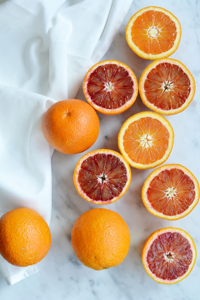 top view image of sliced blood oranges and regular oranges arranged on a surface, some whole oranges are placed beside them