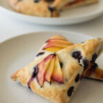 Blueberry and nectarine scones on a stone colored plate with more scones in the background on a white table
