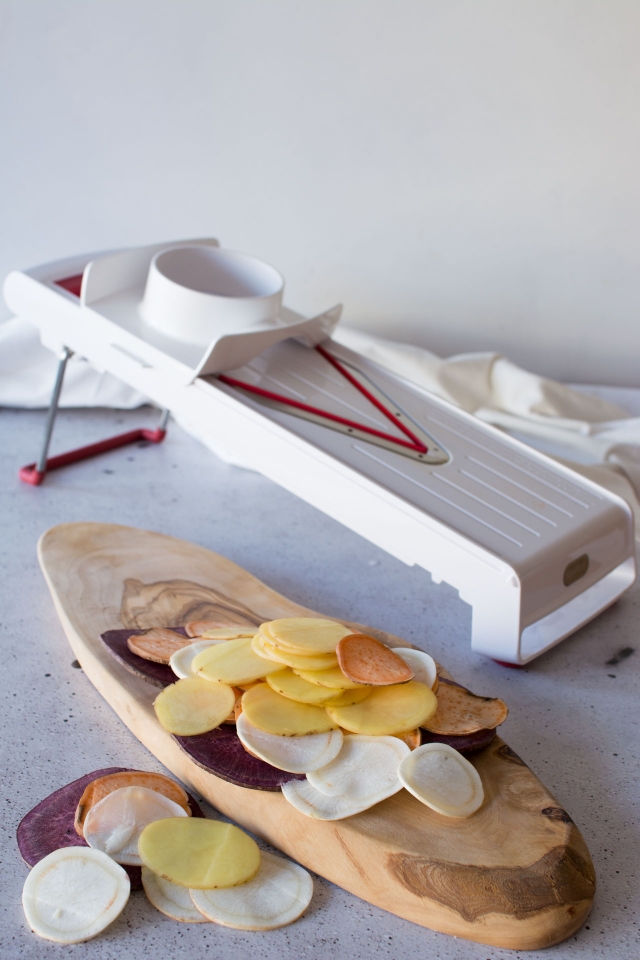 Thinly slice potatoes and a mandolin nearby.