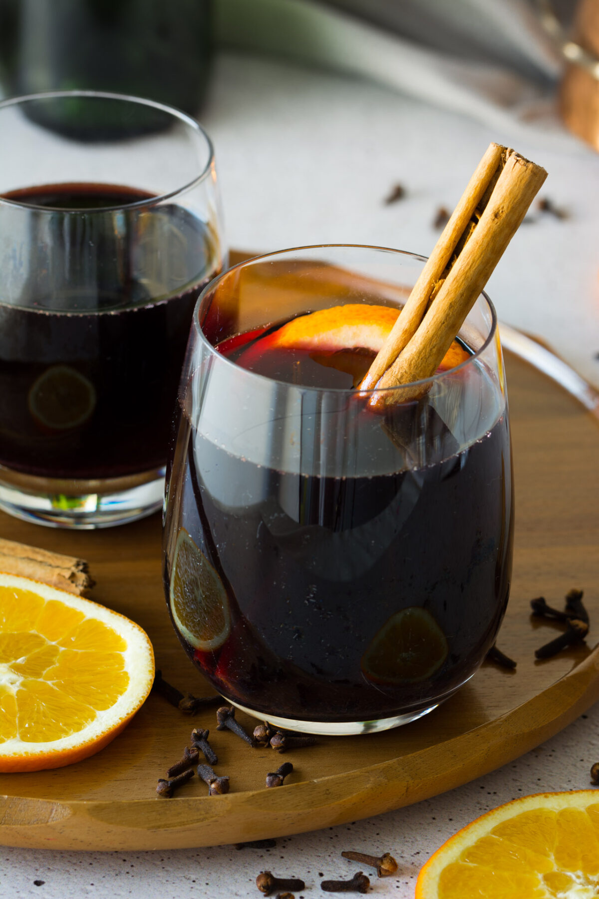 close up image of two glasses of german mulled wine with a cinnamon stick and slices of lemons nearby