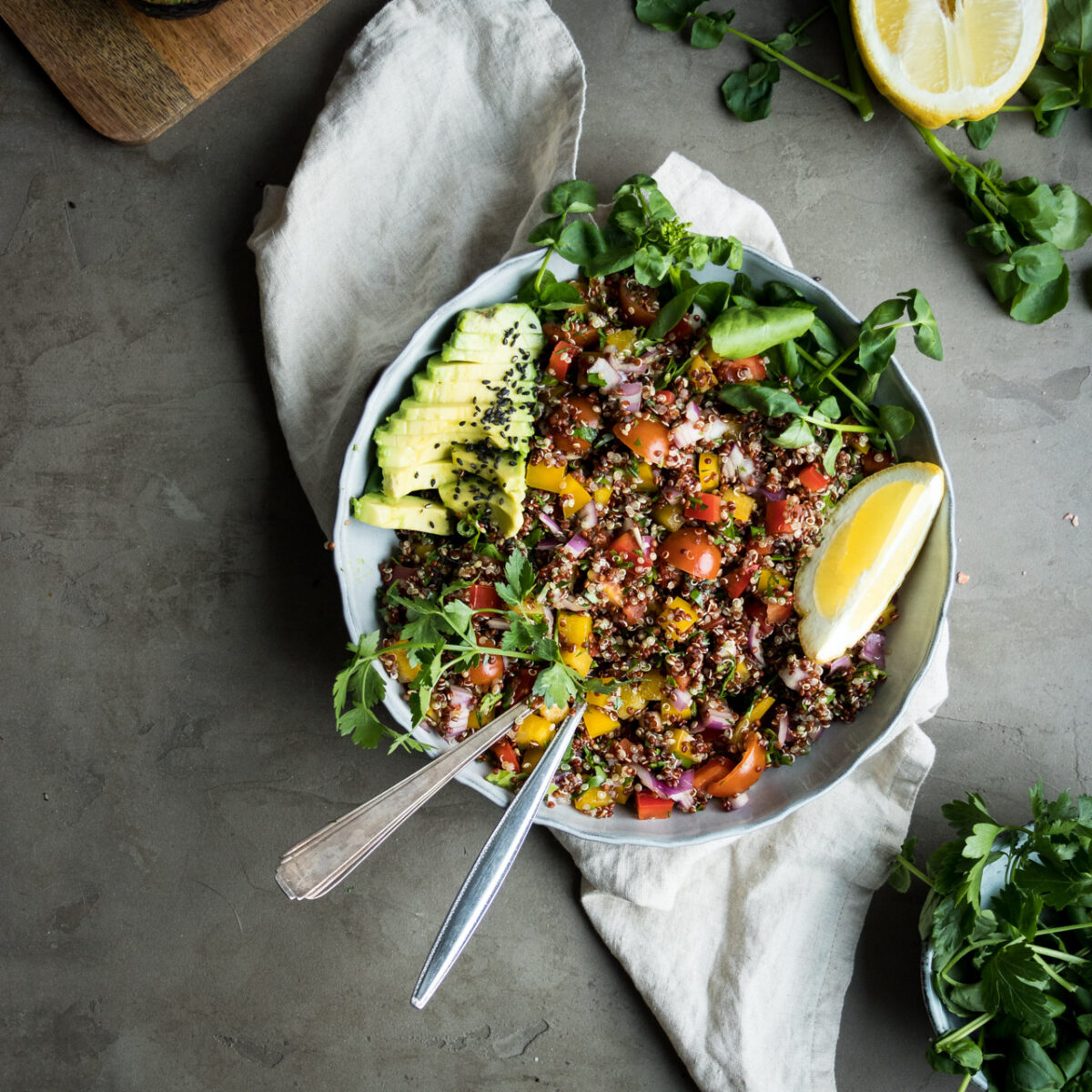 A white bowl filled with a Mediterranean quinoa salad with lemon wedges.