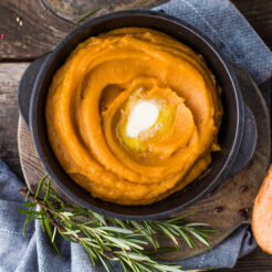 Healthy mashed sweet potato with rosemary in a cast iron saucepan on a table.