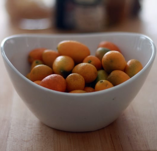 A white bowl filled with kumquats.