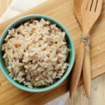 Cooked brown rice in a bowl on a cutting board with wooden utensils.