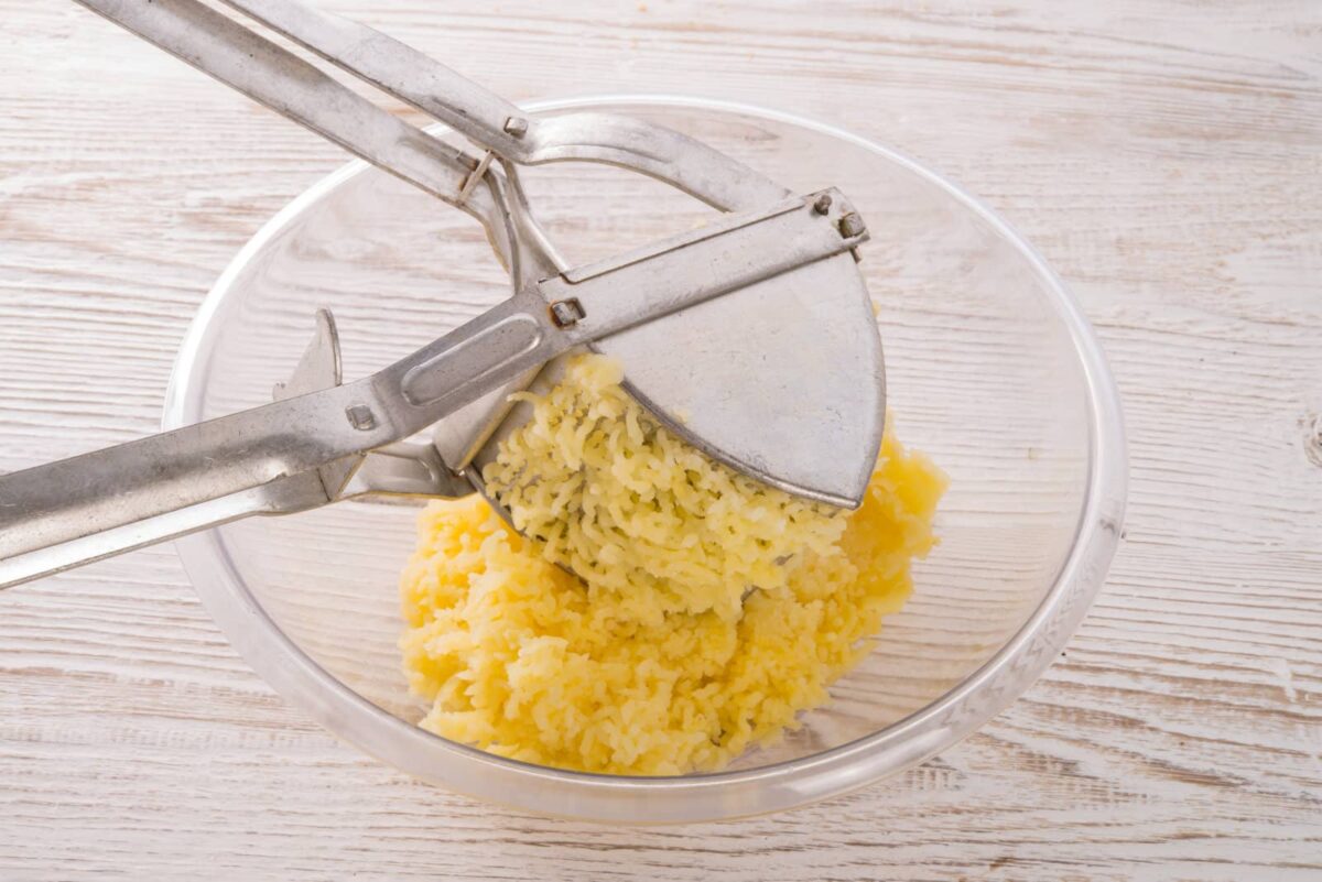 Potato ricer mashing potatoes into a glass bowl.