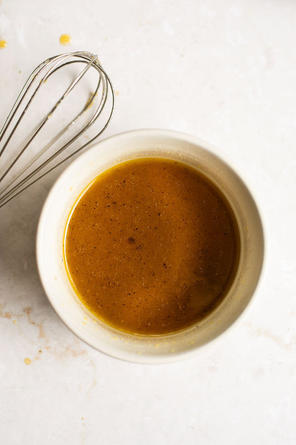 Maple Dijon Dressing in a white bowl with a whisk laying next to it..