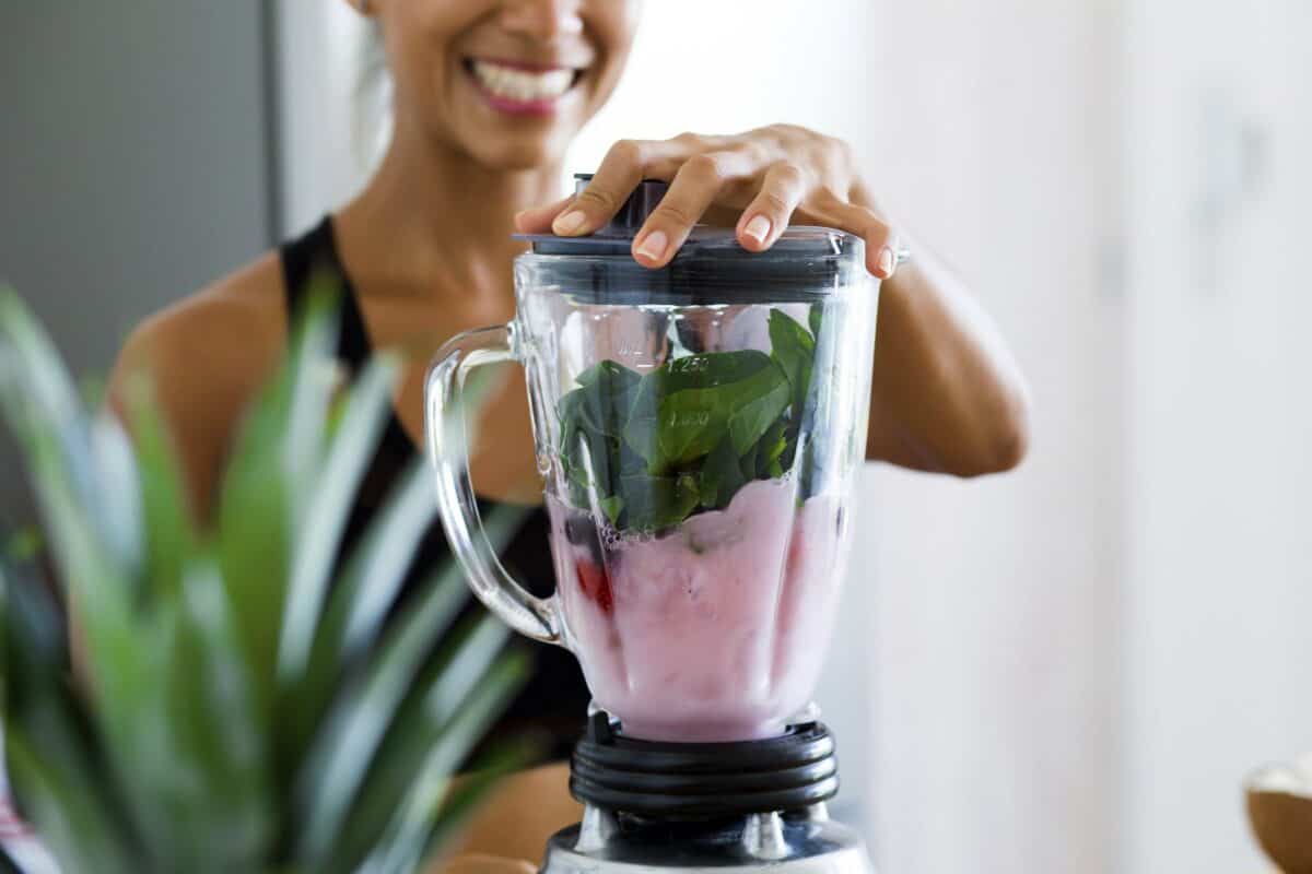 An image of a woman making a smoothie using a blender. 